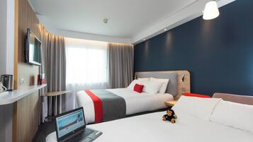 Una habitación de hotel con una cama, un escritorio con una computadora portátil, un televisor y una ventana con cortinas.