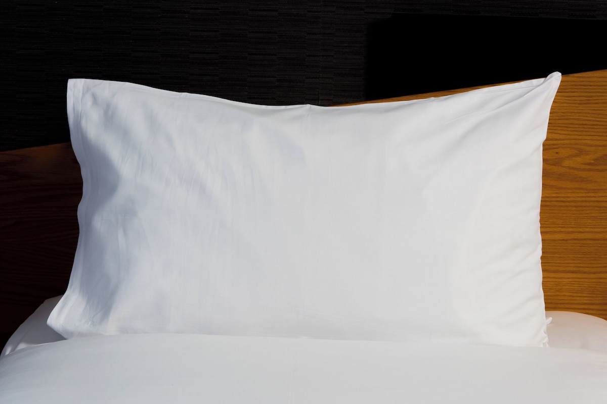 A white pillow on a bed with a wooden headboard.