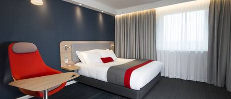 A modern hotel room with a bed, a desk, and a chair.
