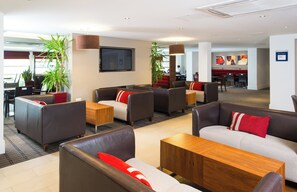 A modern hotel lobby with leather sofas, wooden tables, and potted plants.