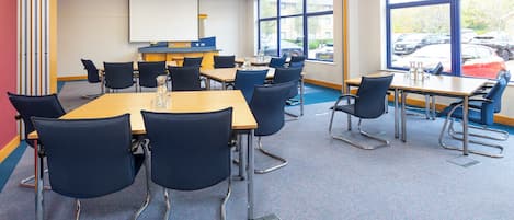 A conference room with a large table, chairs, a projector screen, and large windows with a parking view.