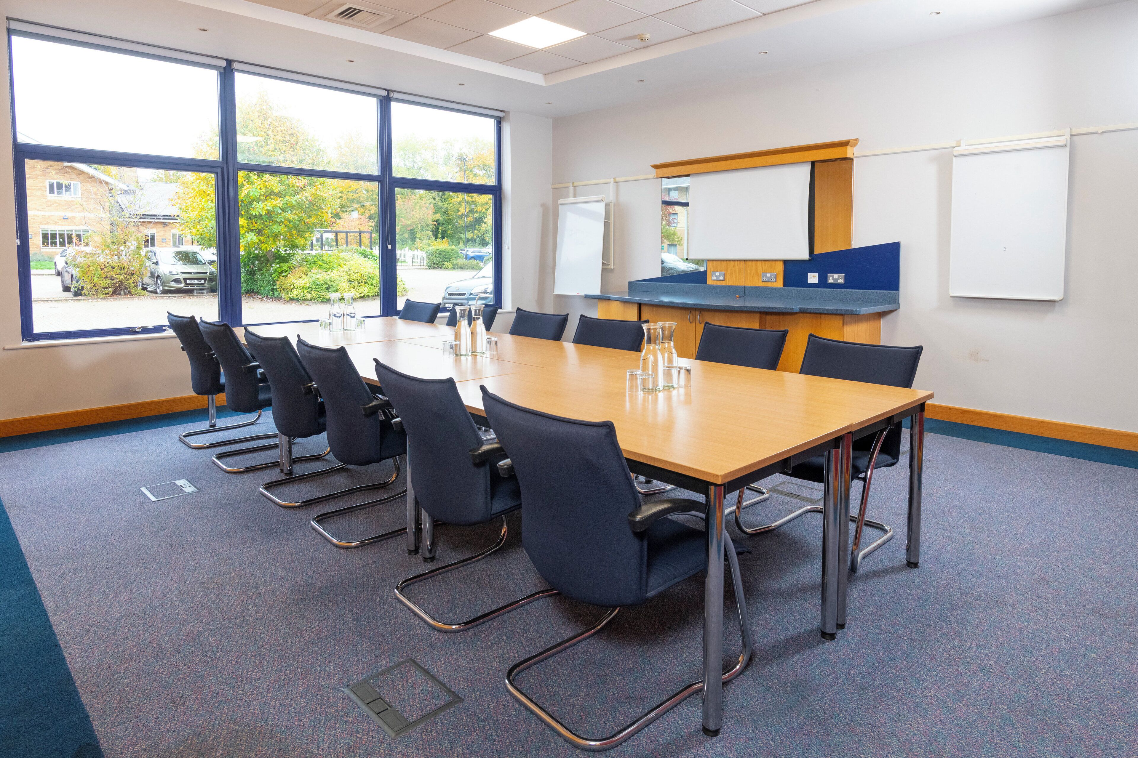 A conference room with a large table, chairs, a whiteboard, and a view of the outside.