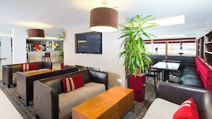 A modern hotel lobby with leather seating, a wooden reception desk, and a large potted plant. - Holiday Inn Express Milton Keynes by IHG (Milton Keynes)