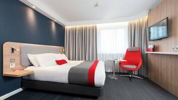 Habitación de hotel con cama, mesita de noche, silla, televisor y cortinas.