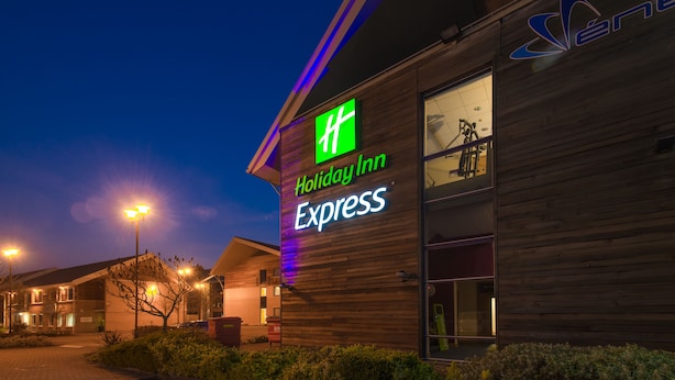 A Holiday Inn Express building with a prominent green and white logo, large windows, and a wooden facade. - Holiday Inn Express Milton Keynes by IHG (Milton Keynes)