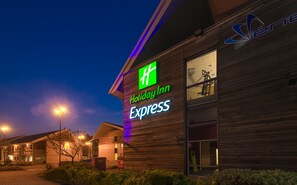 Edifício Holiday Inn Express com logotipo verde e branco bem visível, grandes janelas e fachada de madeira.