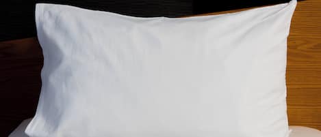 A white pillow on a bed with a wooden headboard.