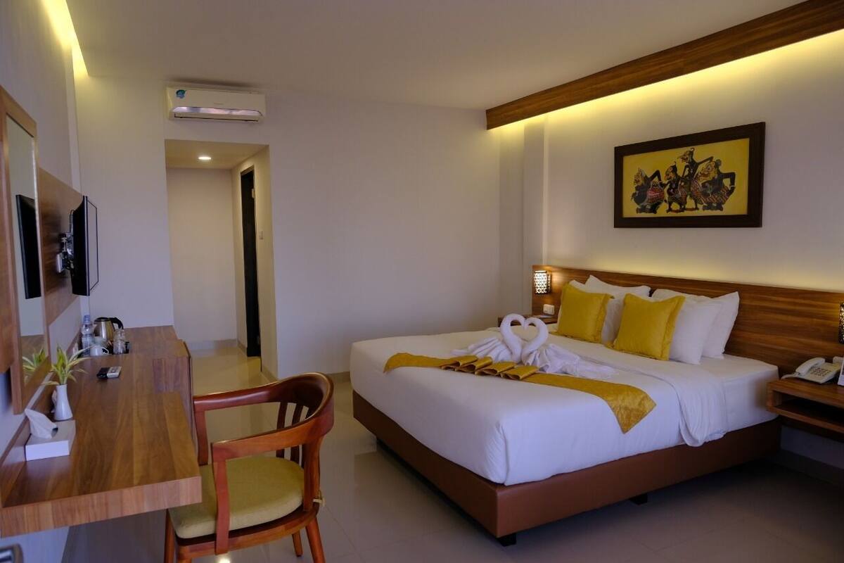 A hotel room with a bed, a desk, a chair, a bedside table with a lamp, and a wall-mounted TV.
