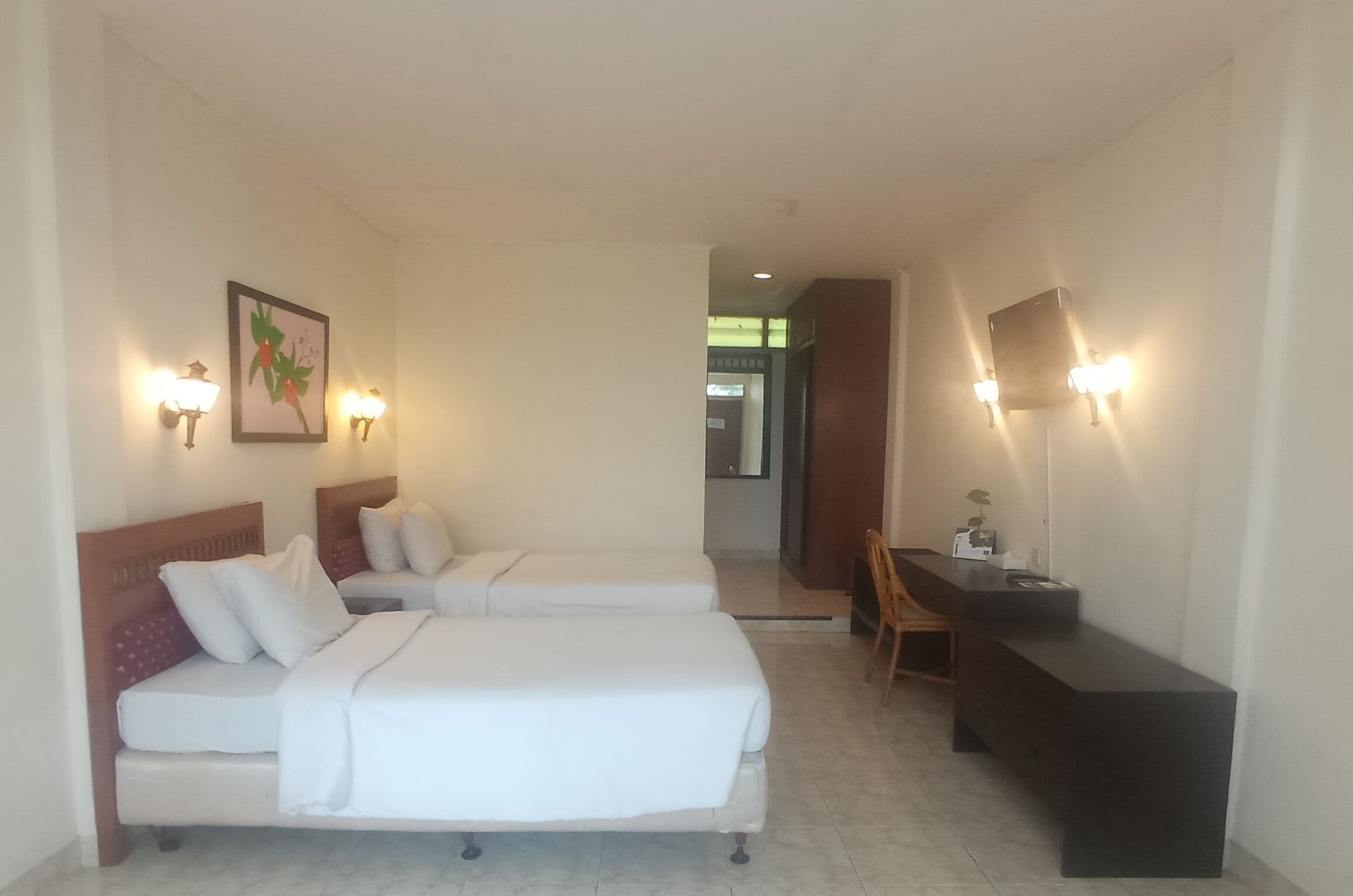Habitación de hotel con dos camas, un escritorio e iluminación en la pared.