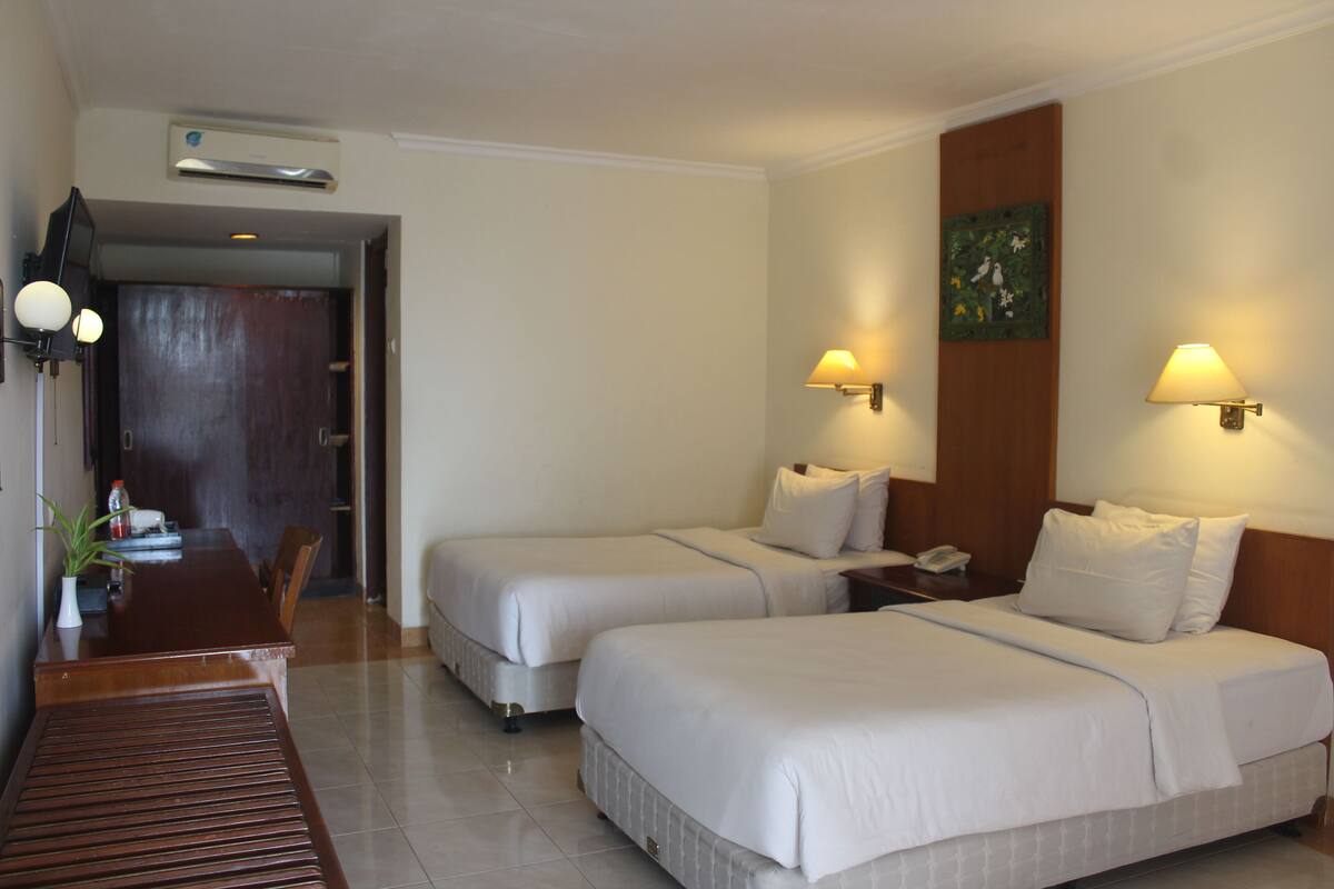 A hotel room with two beds, a wooden dining table, and a small table with a plant.