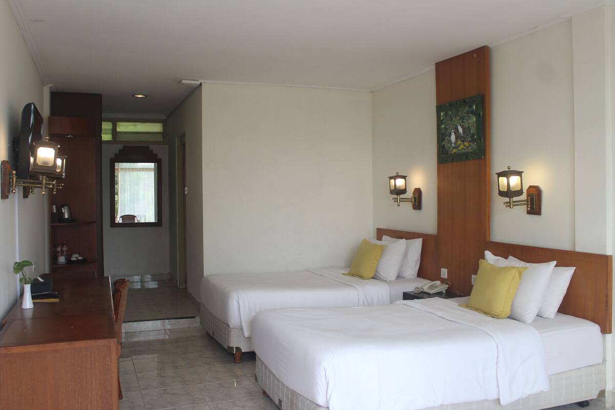 A hotel room with two beds, a desk, and a chair. There are wall-mounted lamps and a painting on the wall.