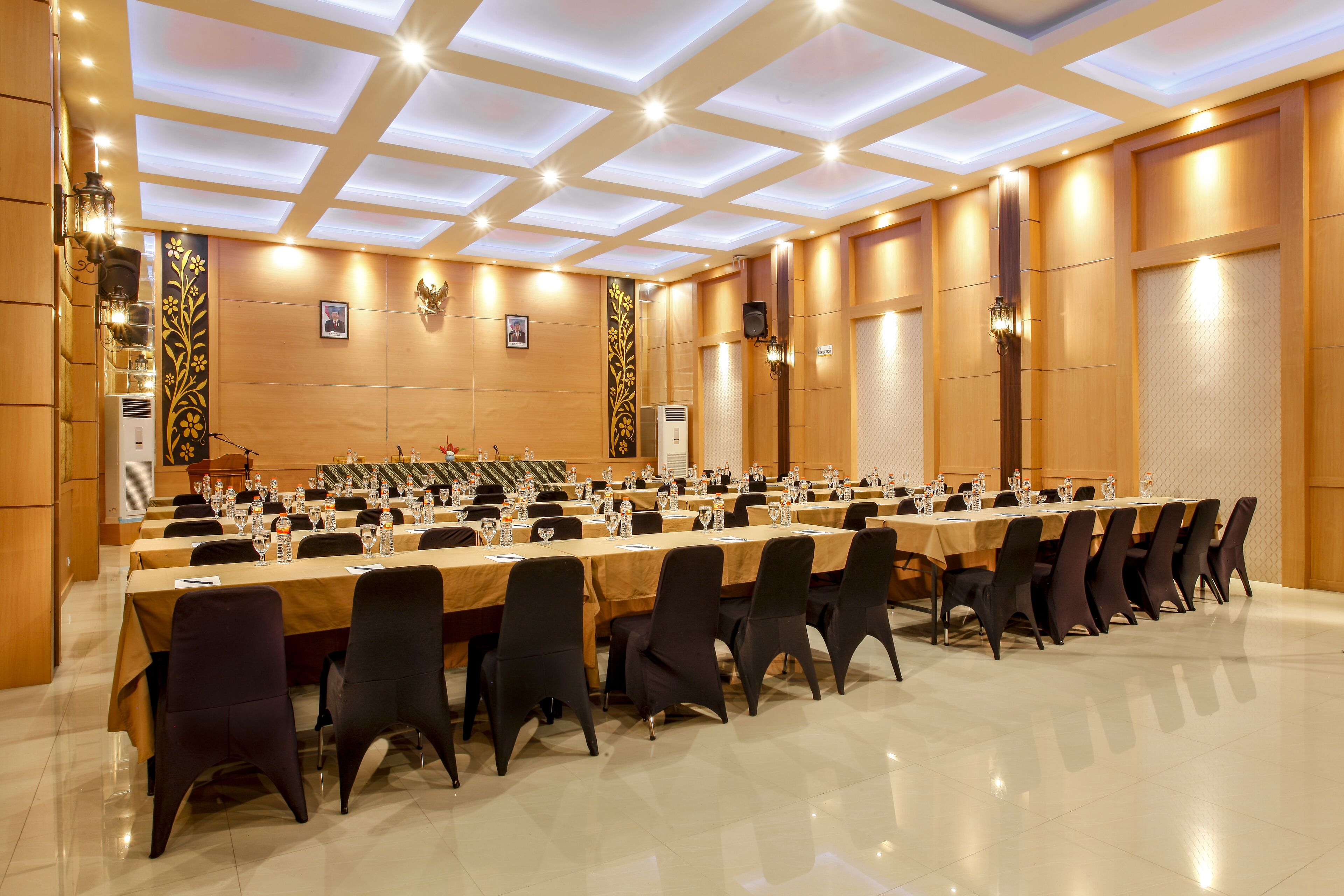 Un salón de conferencias con largas mesas, sillas y un escenario.