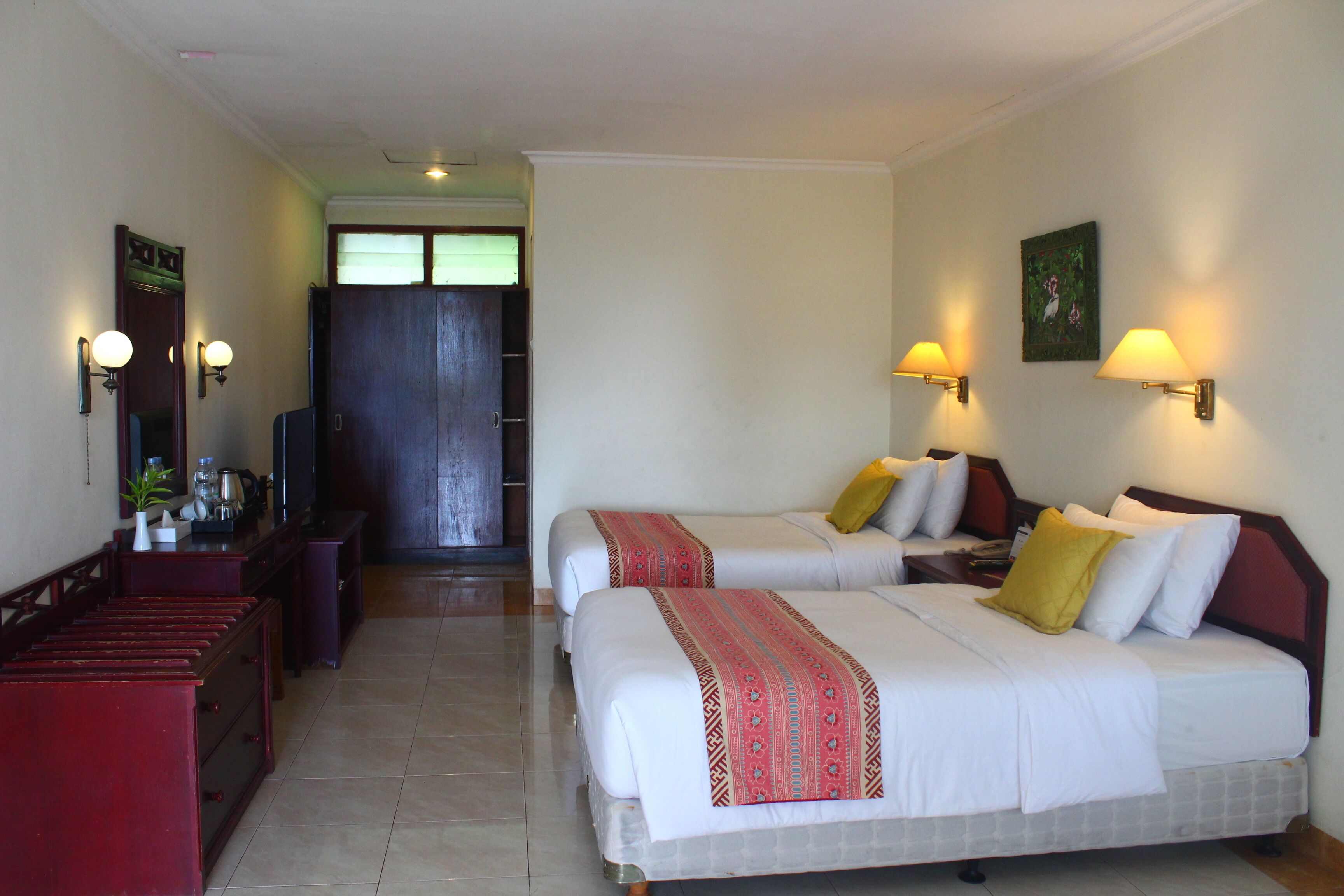 A hotel room with two beds, a desk with a chair, a TV, and a door leading to another room.