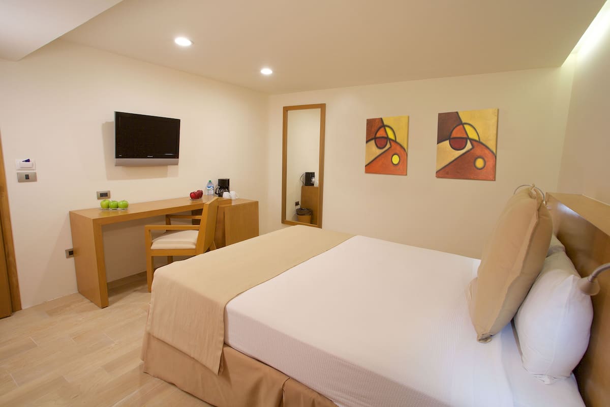 Una habitación de hotel con cama, escritorio, silla, televisión y obras de arte en las paredes.