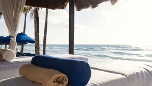 A beachside bed with a view of the ocean, a thatched roof, and blue umbrellas. - Hotel NYX Cancun - Near La Isla Shopping Mall (Cancun)