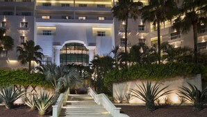 A multi-story hotel with a central entrance, palm trees, and a well-lit staircase. - Hotel NYX Cancun - Near La Isla Shopping Mall (Cancun)
