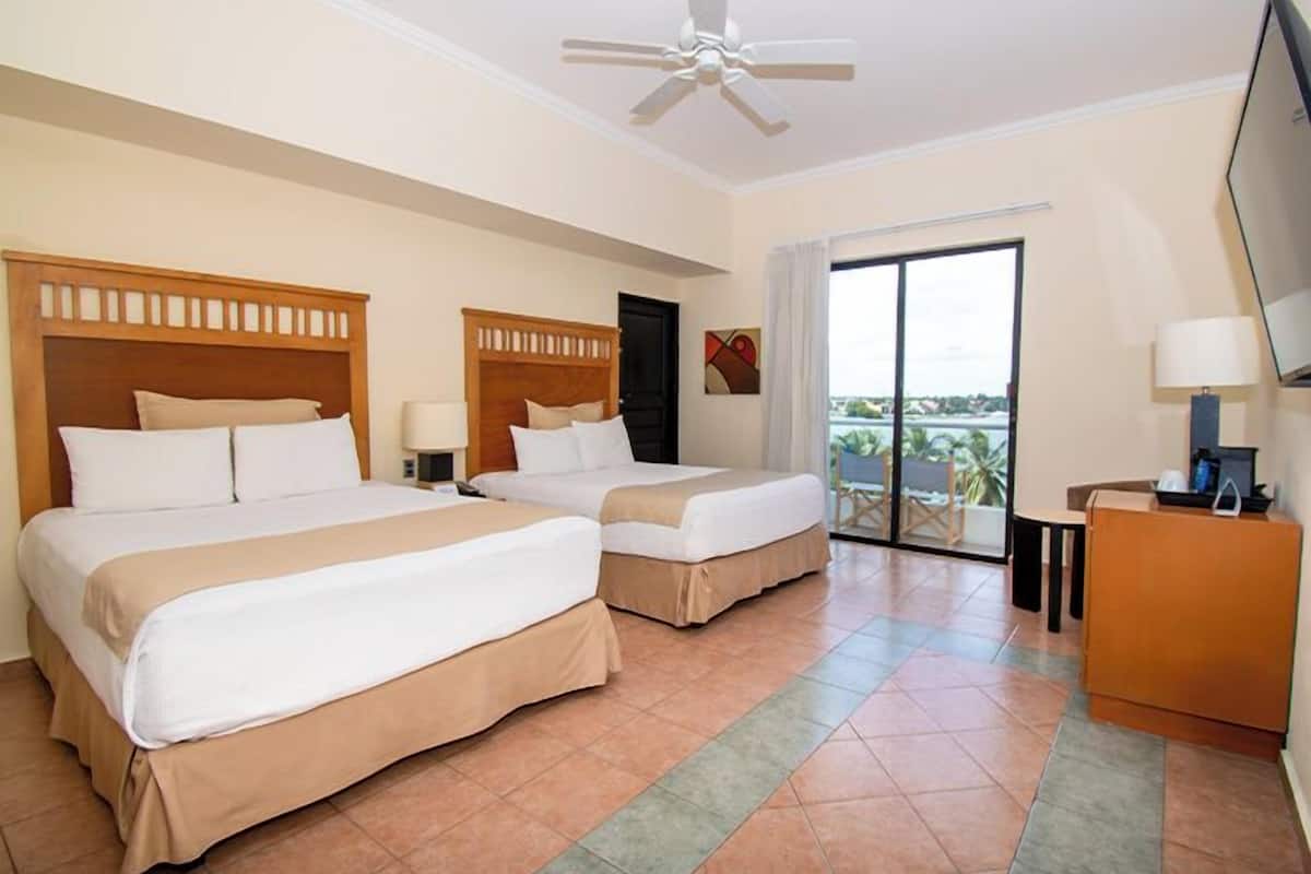 Habitación de hotel con dos camas, ventilador de techo, televisor y balcón con vistas.