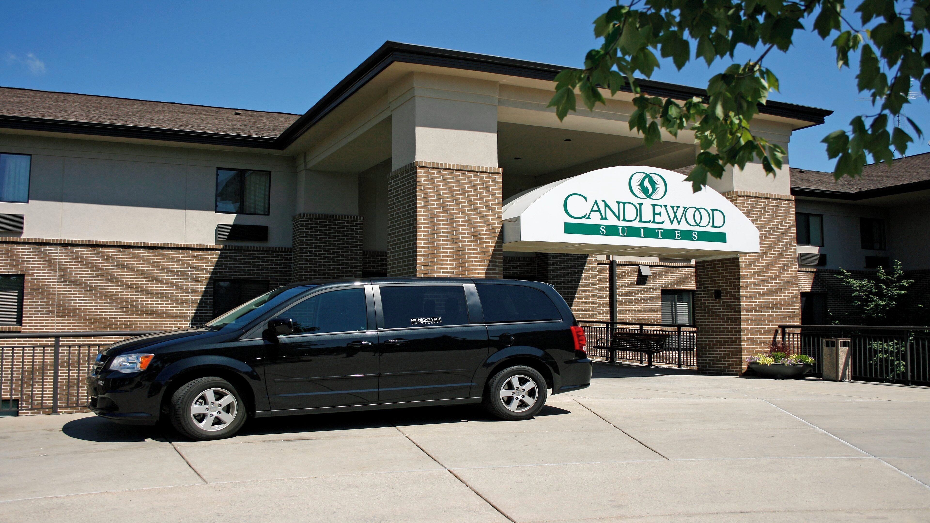 Un edificio con un cartel que dice 'Candlewood Suites' y un vehículo estacionado en la parte delantera.