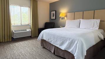 Habitación de hotel con una cama grande, una silla, una lámpara de pared y una ventana con cortinas.