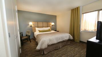 A hotel room with a bed, a chair, a desk with a television, and two wall-mounted lamps.