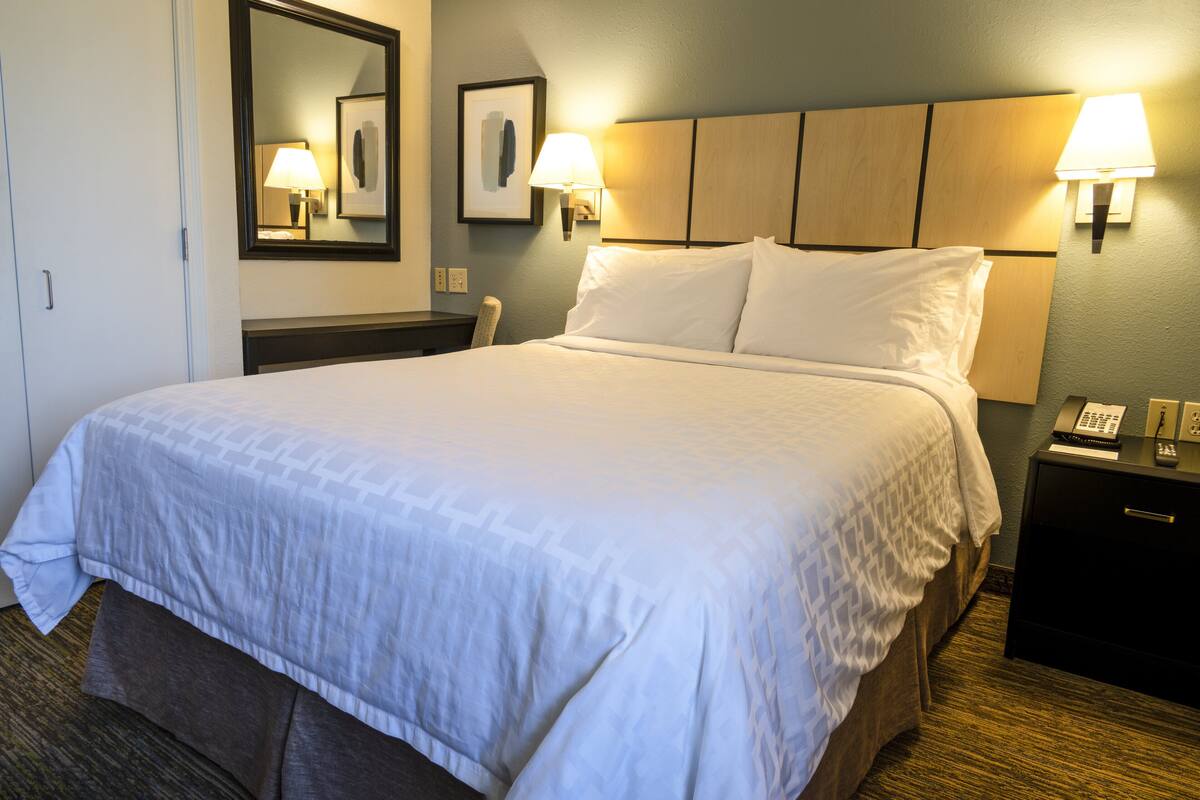 Una habitación de hotel con una cama grande, dos lámparas de noche, una mesita con un teléfono y un espejo en la pared.