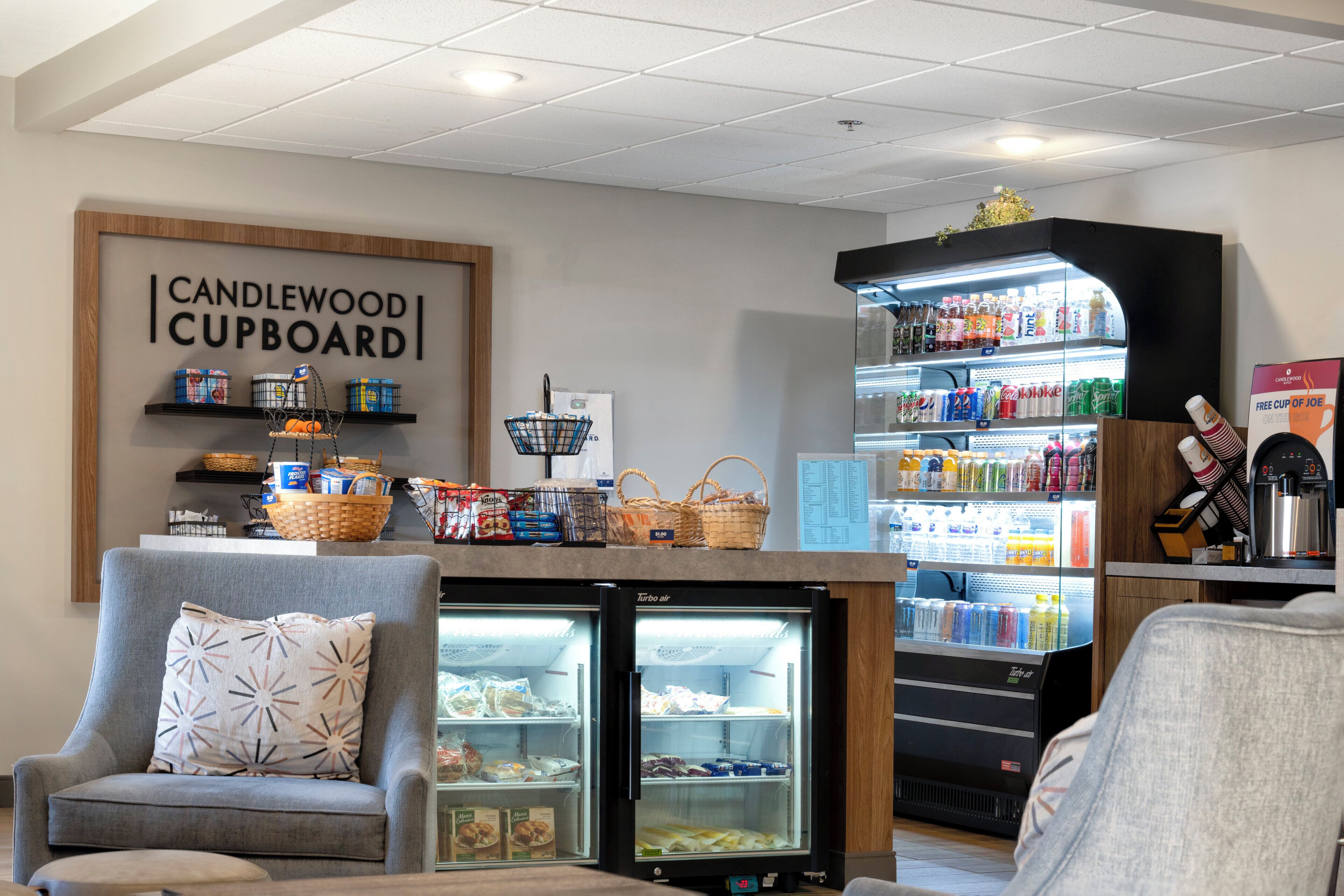 Un área de estar con un sofá y sillones, un expositor refrigerado con aperitivos y un refrigerador para bebidas.