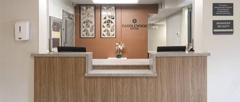Un comptoir d’accueil avec un revêtement en bois, une enseigne indiquant « Candlewood Suites » et une autre indiquant « Responsable de service présent ».