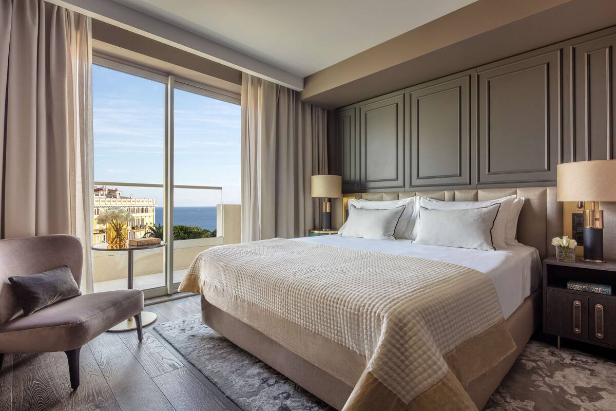 A hotel room with a large bed, a sofa, a nightstand, and a view of the sea.