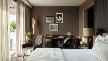 Habitación de hotel con cama, dos sillones, escritorio, lámpara y cuadros en la pared.