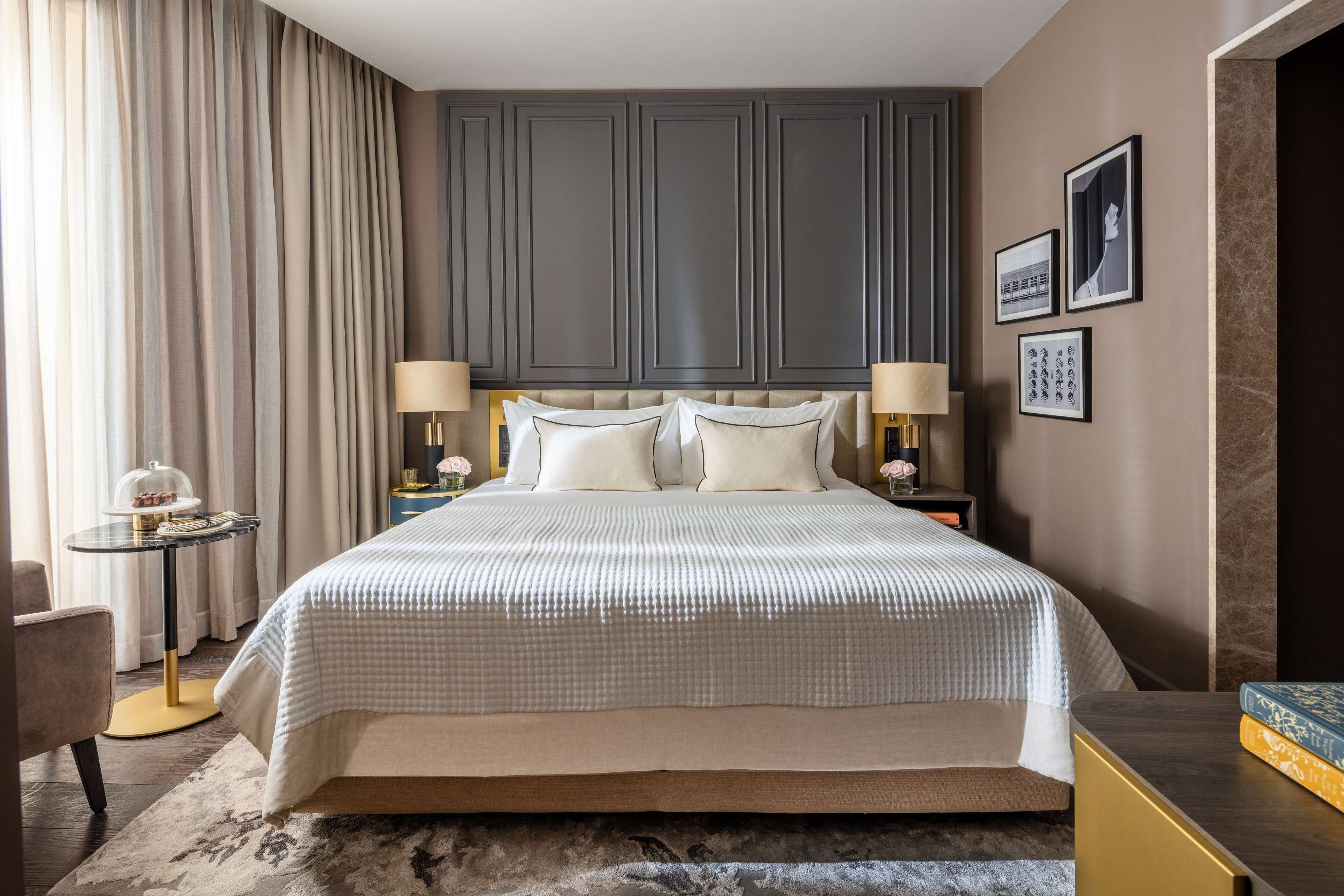 A hotel room with a large bed, two bedside tables with lamps, a small round table with a decorative item, and a chair.