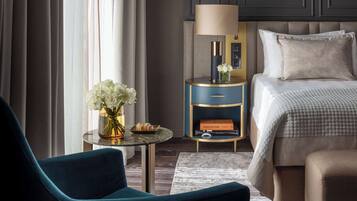 Habitación de hotel con una cama, una mesita de noche con lámpara, un jarrón con flores y una silla.