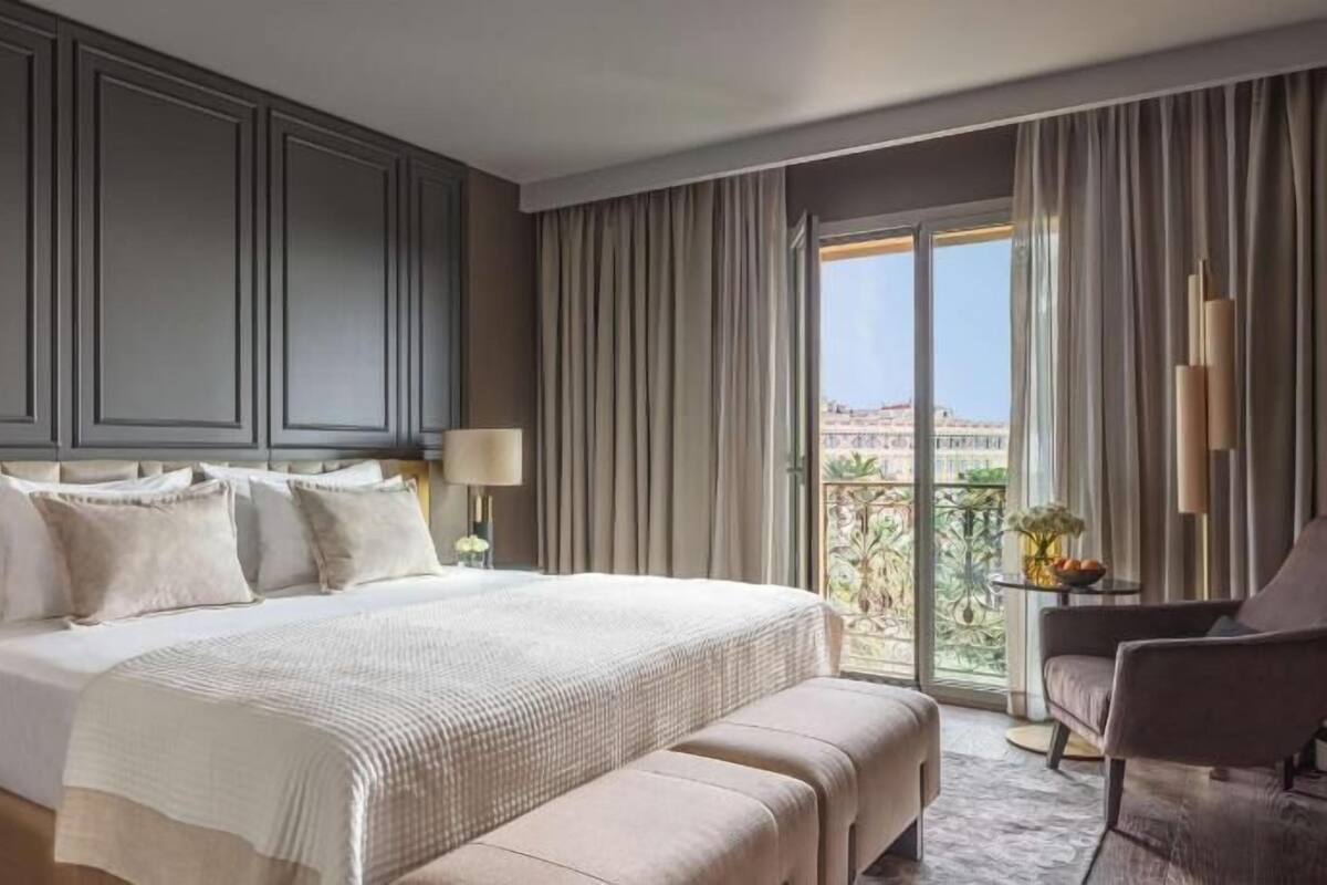 A hotel room with a large bed, a sitting area, and a balcony with a view.