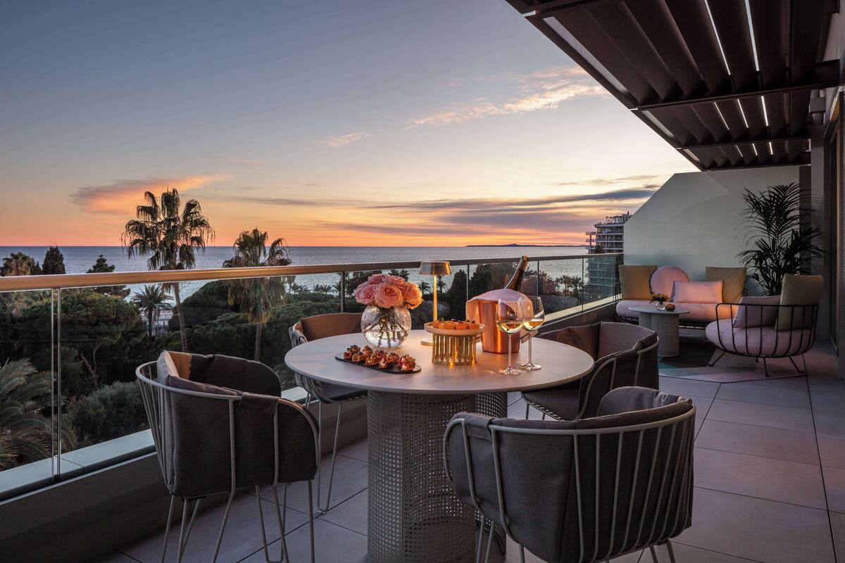 A balcony with a table set for two, a vase of flowers, and a bottle of champagne.