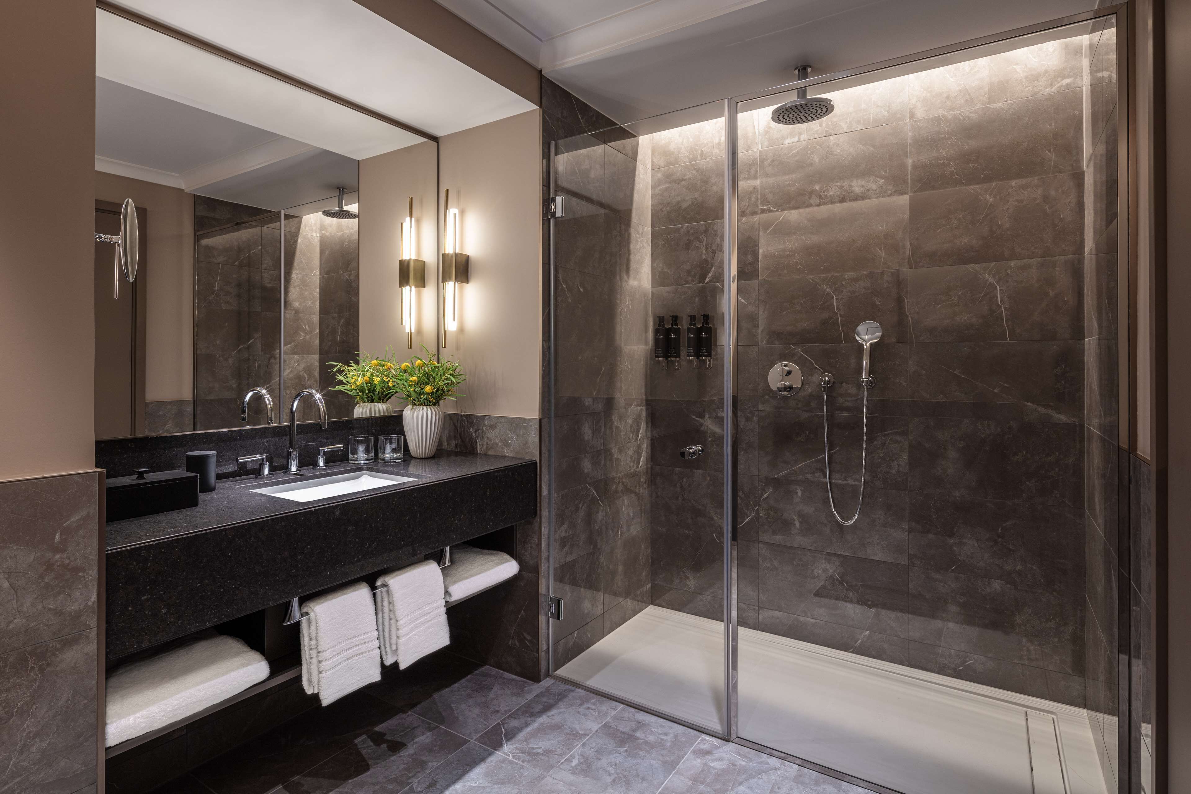 Une salle de bain moderne avec une douche à parois de verre, un grand miroir et un plan de toilette en marbre foncé.