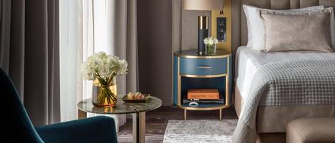 A hotel room with a bed, a nightstand with a lamp, a vase with flowers, and a chair.
