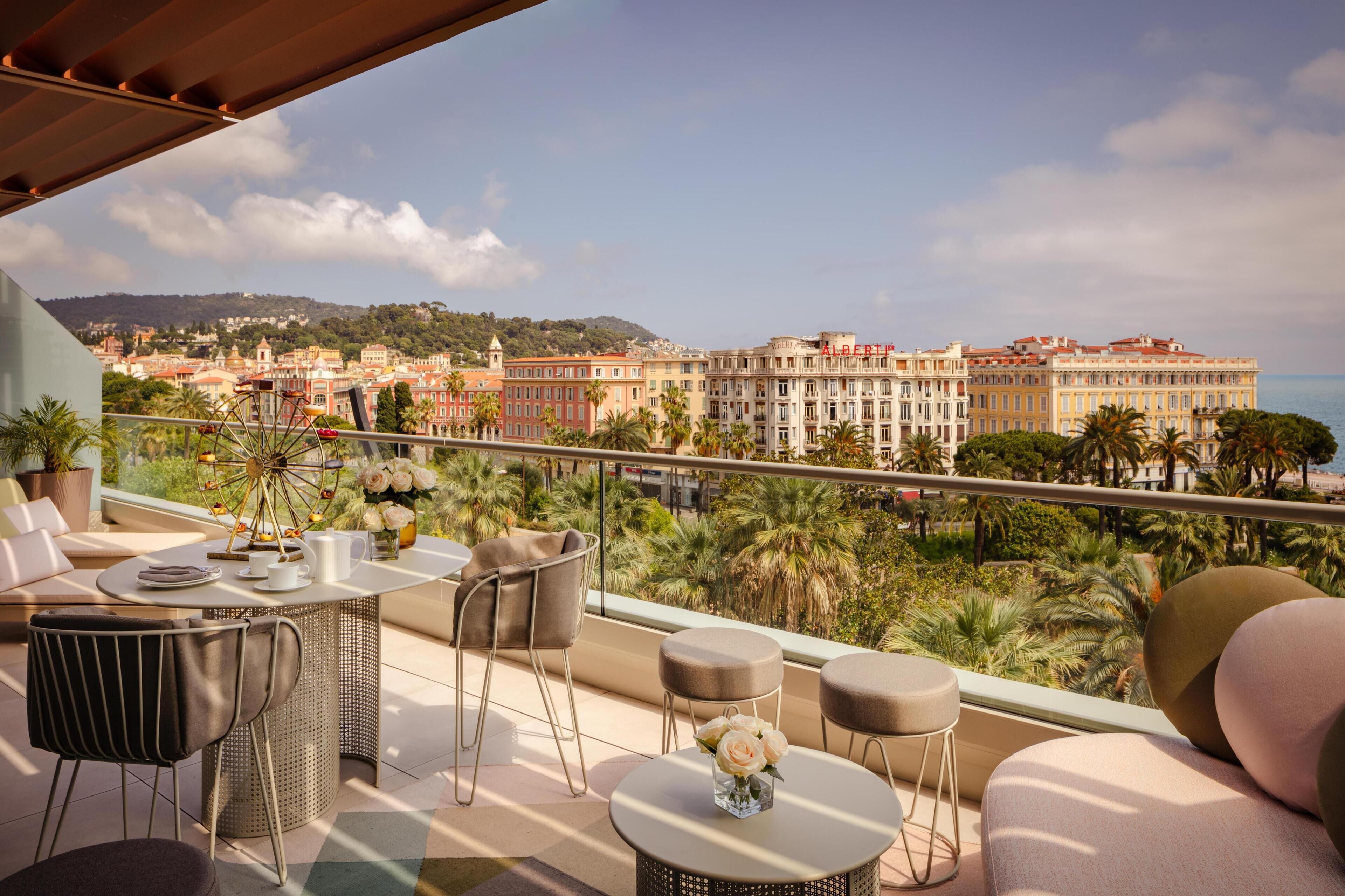 A balcony with a view of a historic building, palm trees, and a Ferris wheel.