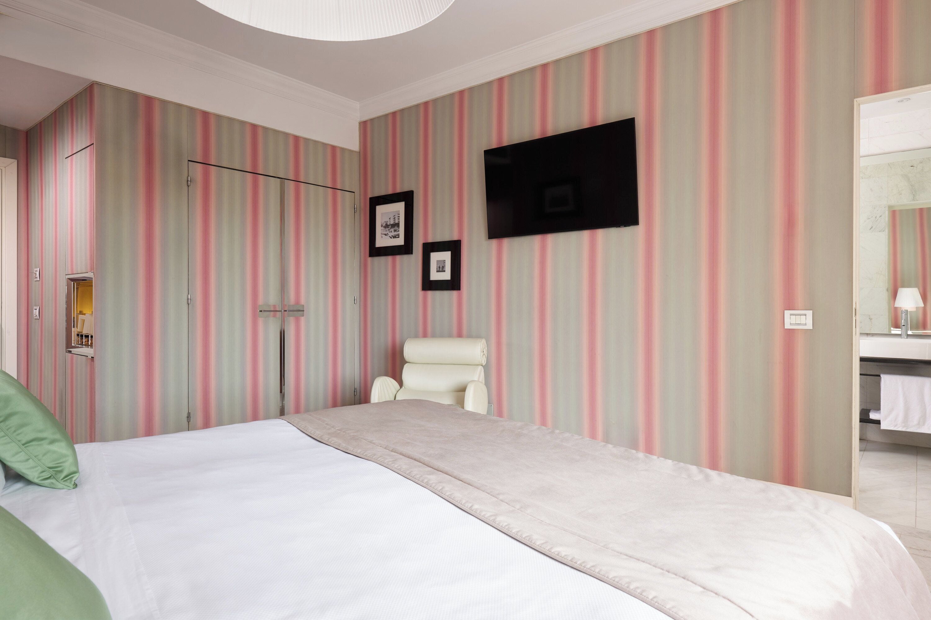 Habitación de hotel con cama, una silla, televisor y baño visible a través de una puerta abierta.