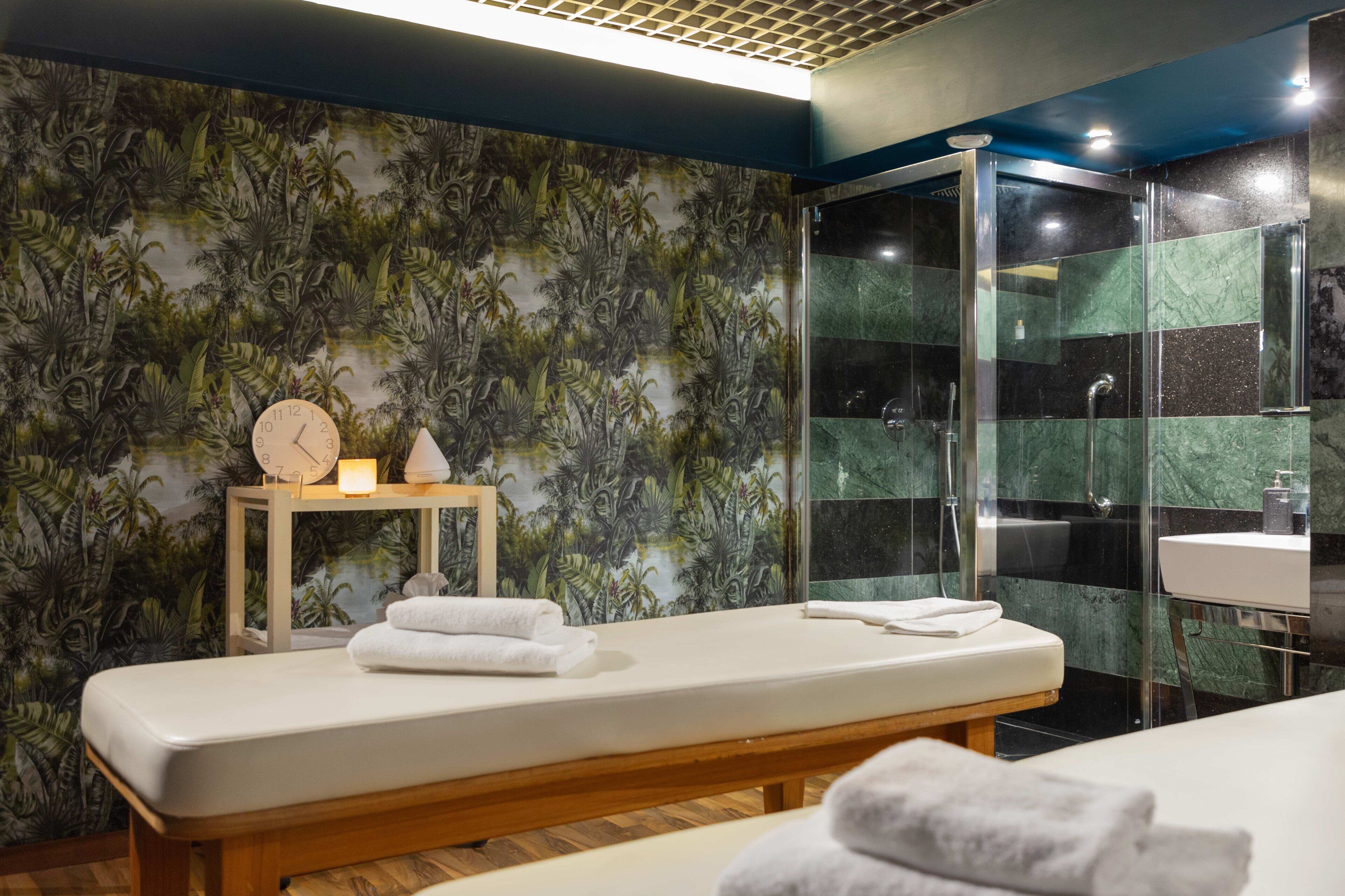 A modern bathroom with a wooden bench, a glass shower enclosure, and a wall with a tropical leaf pattern.