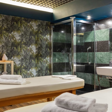 A modern bathroom with a wooden bench, a glass shower enclosure, and a wall with a tropical leaf pattern.