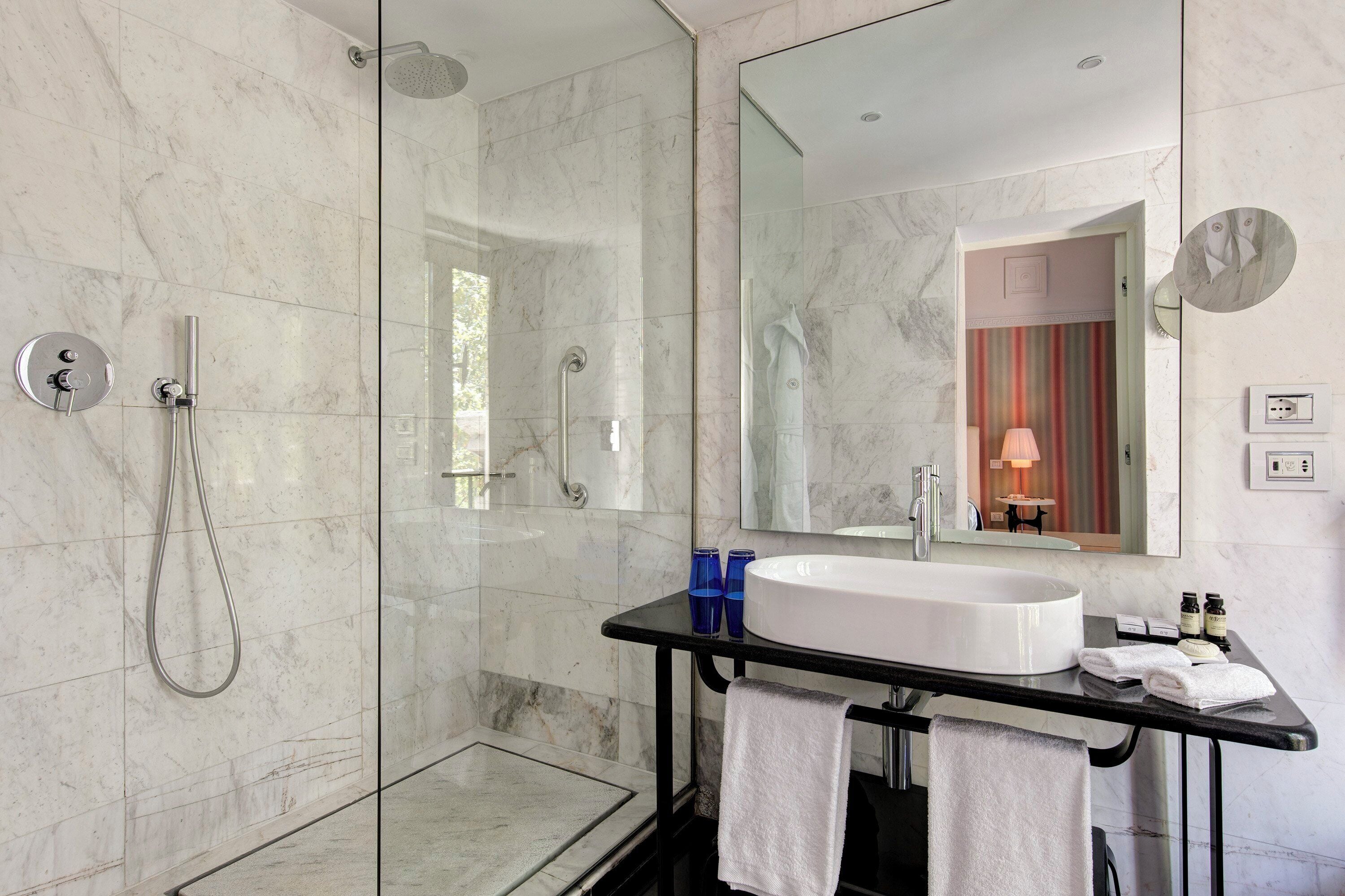 Un baño moderno con ducha envuelta en vidrio, un lavamanos grande de color blanco y un espejo sobre él.