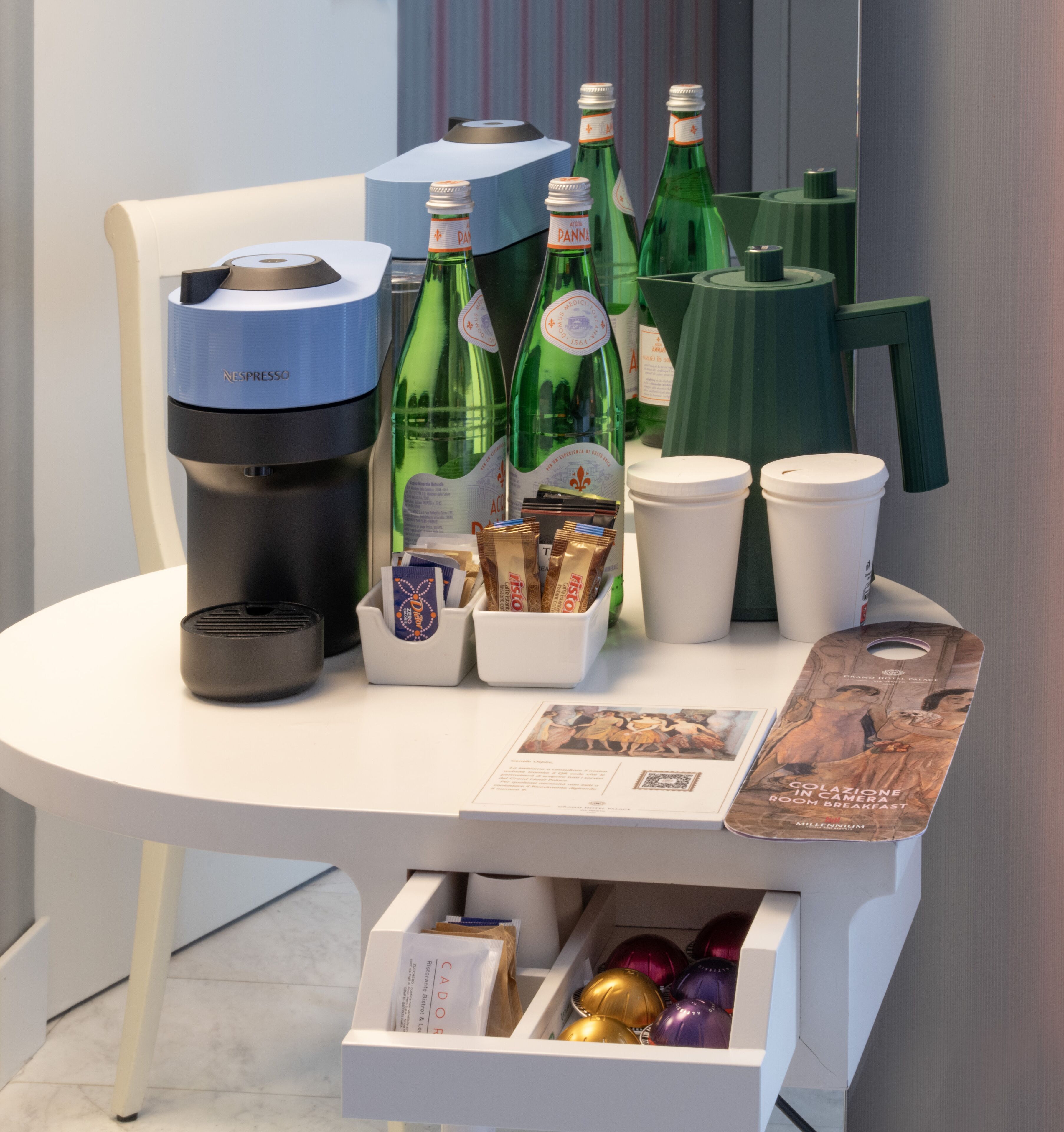 A table with a Nespresso machine, green bottles, coffee cups, and a brochure.