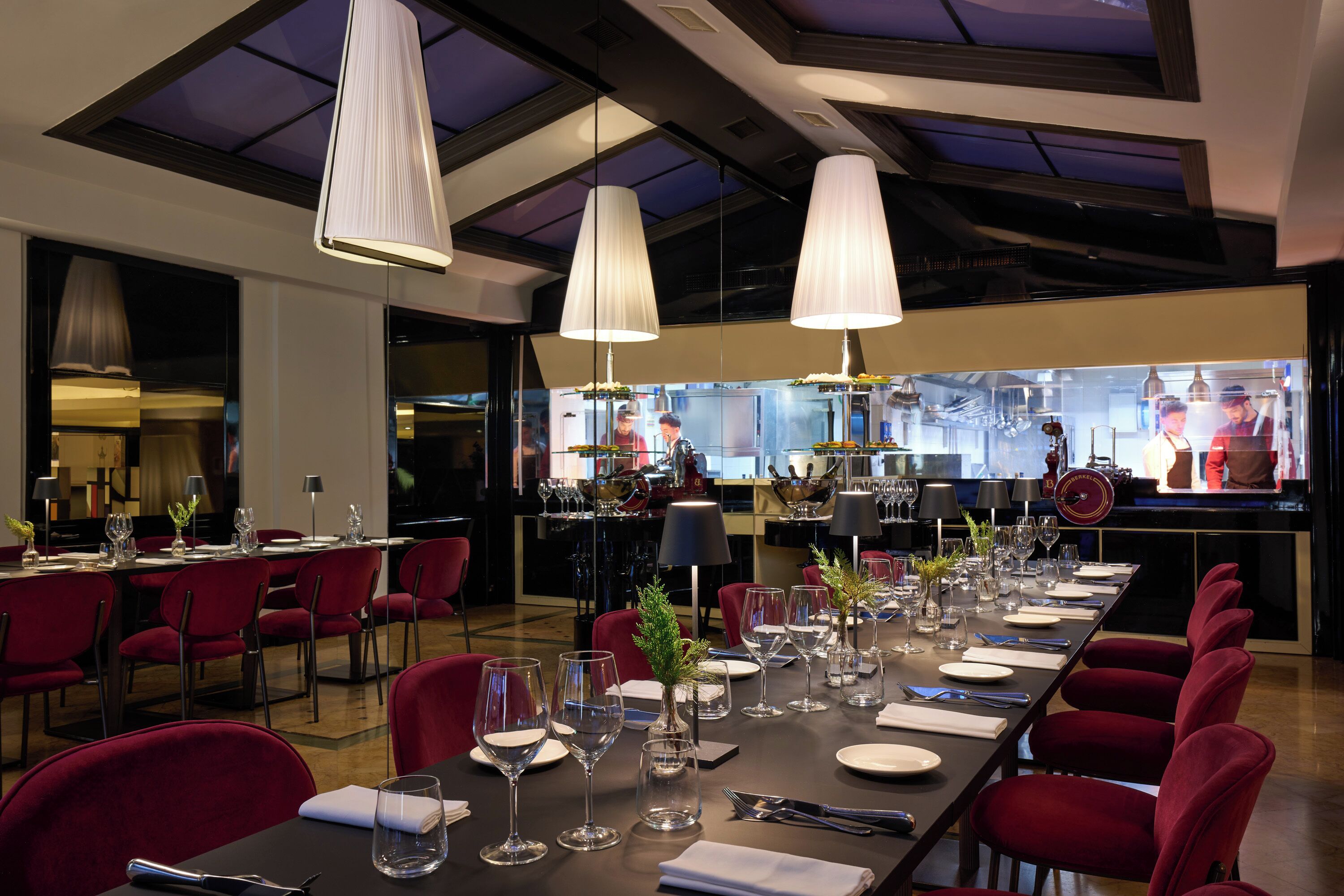 A restaurant with a long dining table set for a meal, red chairs, and overhead pendant lighting.