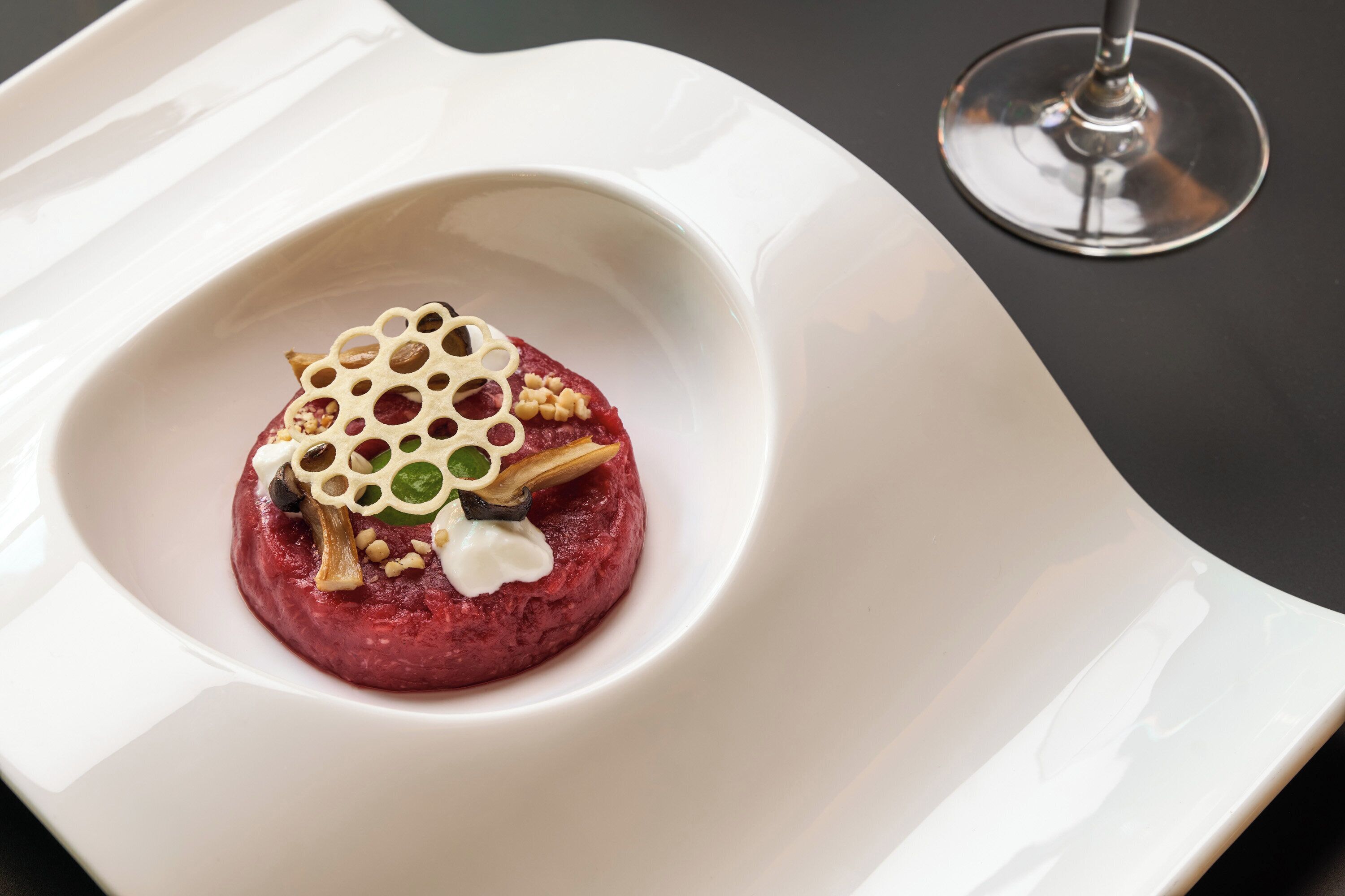 Un plato blanco con un alimento rojo, adornado con nueces y un detalle decorativo, sobre una superficie oscura.