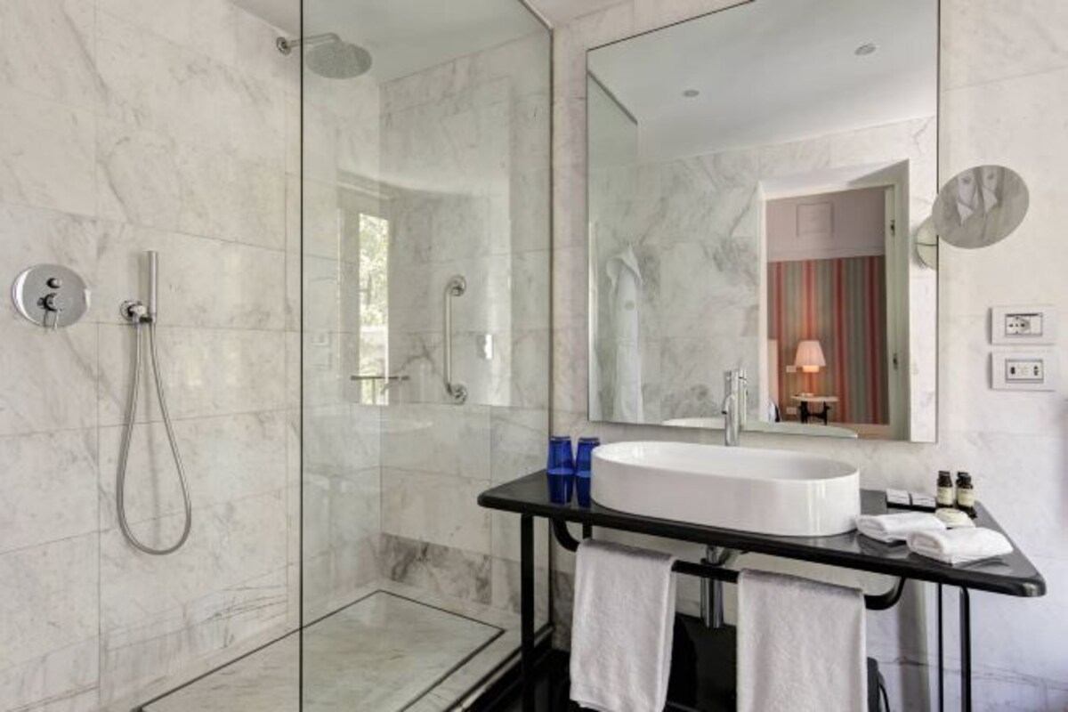 A modern bathroom with a glass-enclosed shower, a large mirror, a white sink, and a black countertop.