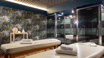 Un cuarto de spa con dos camillas de masaje, una zona de ducha y una pared con un diseño de hojas tropicales.