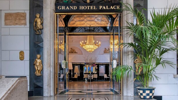 The entrance of Grand Hotel Palace with a grand arched doorway, a chandelier, and a potted plant. - Grand Hotel Palace Rome (Rome)