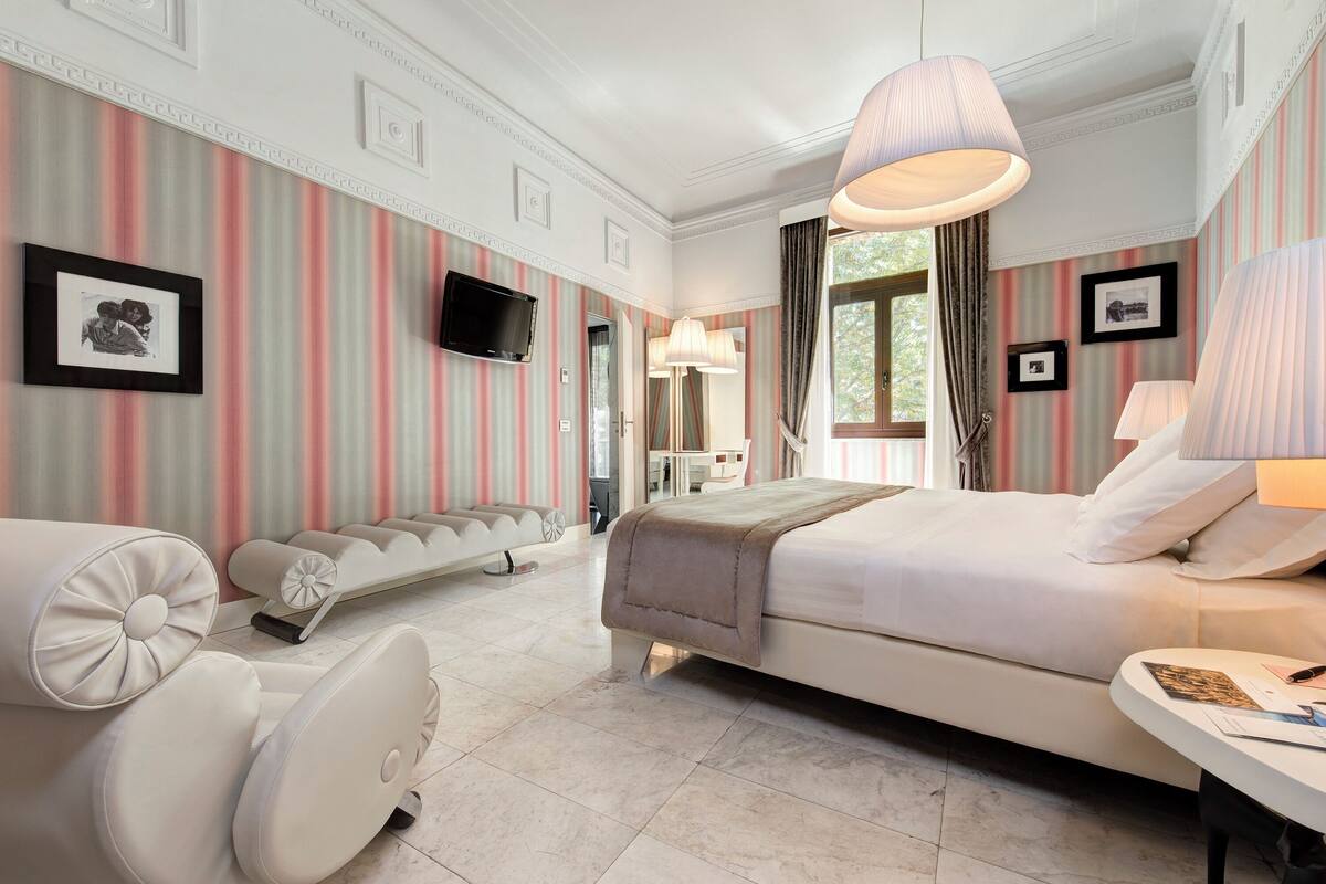 A modern hotel room with a large bed, a sofa, a desk, and a television.