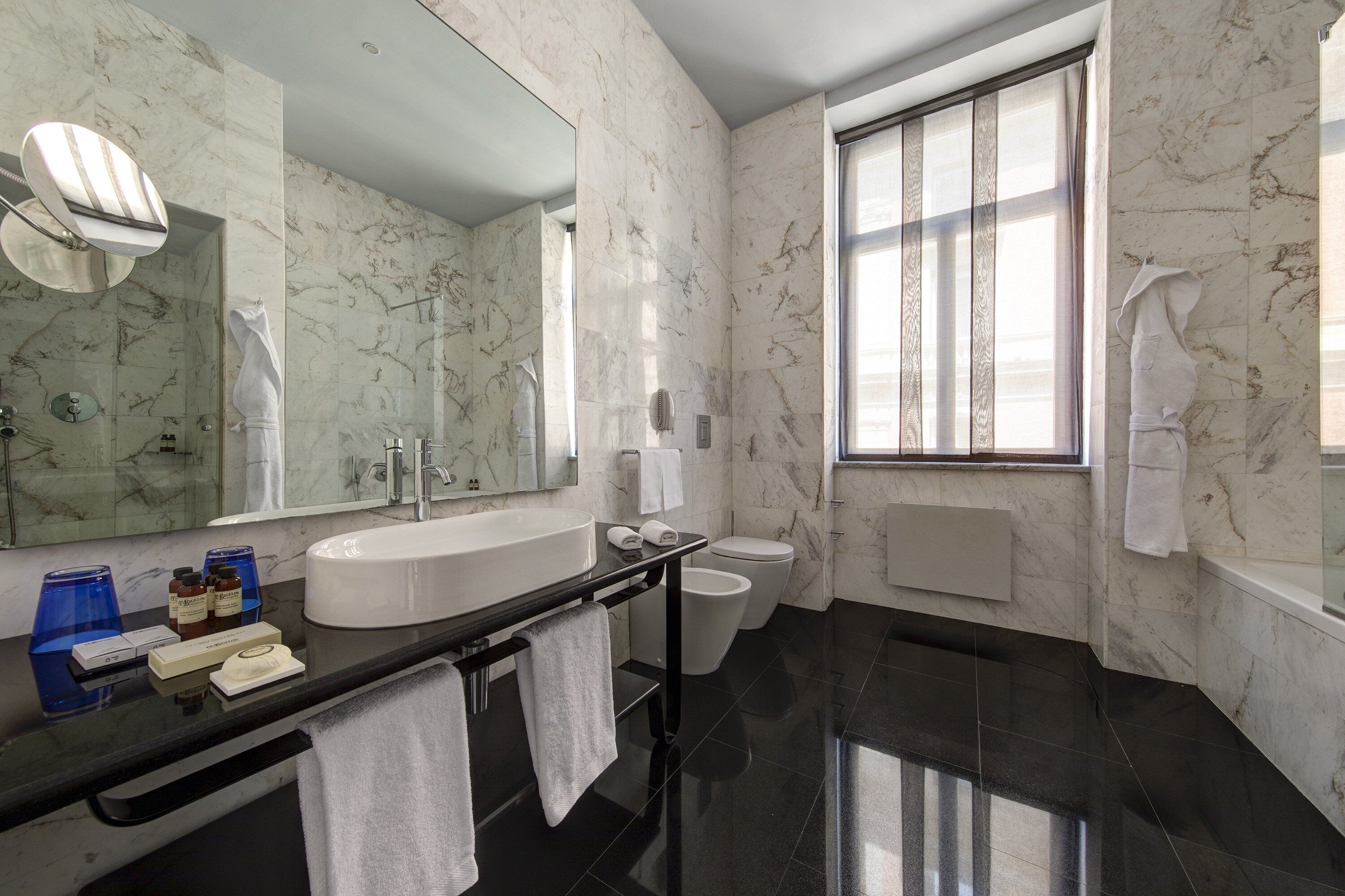 Une salle de bain moderne avec un grand miroir, une baignoire, des toilettes et un lavabo.