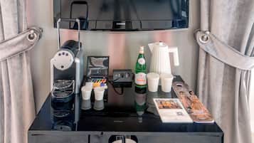 Un mini-frigo con una macchina del caffè, bottiglie, tazze e una rivista.