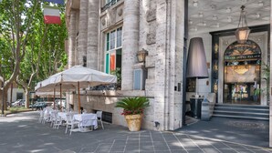 A grand hotel entrance with a large archway, a flag, and outdoor seating with umbrellas. - Grand Hotel Palace Rome (Rome)